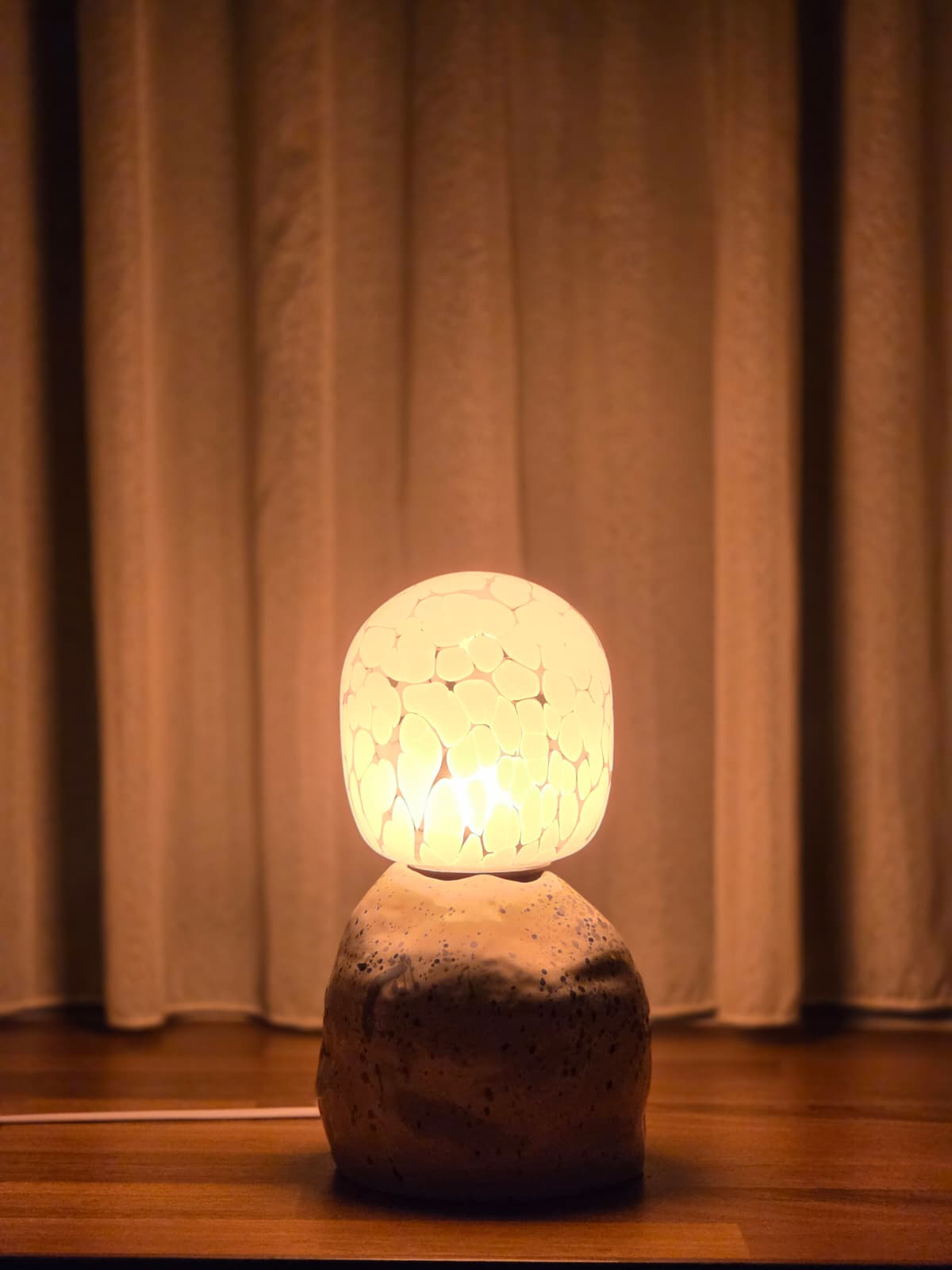 Ceramic table lamp glowing warmly against linen curtains