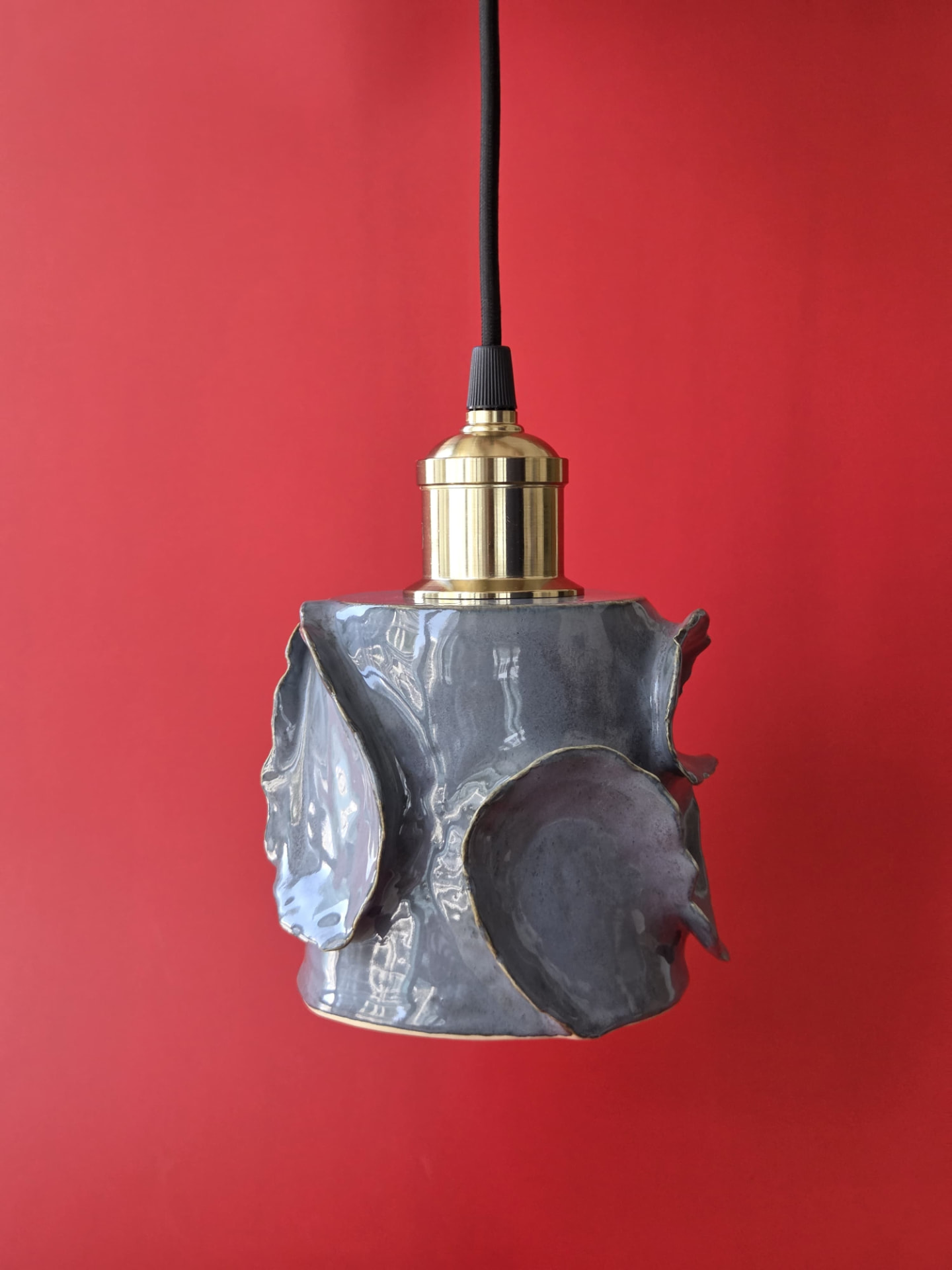 Tidal, a dark-glazed stoneware pendant light with overlapping organic forms and brass furnishing against a red backdrop