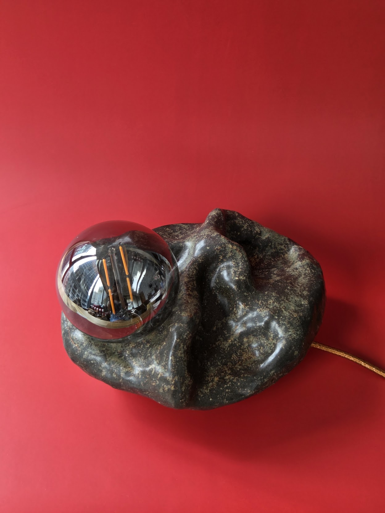 Overhead view of Shoal's undulating dark stoneware form with its smoked glass globe resting within it
