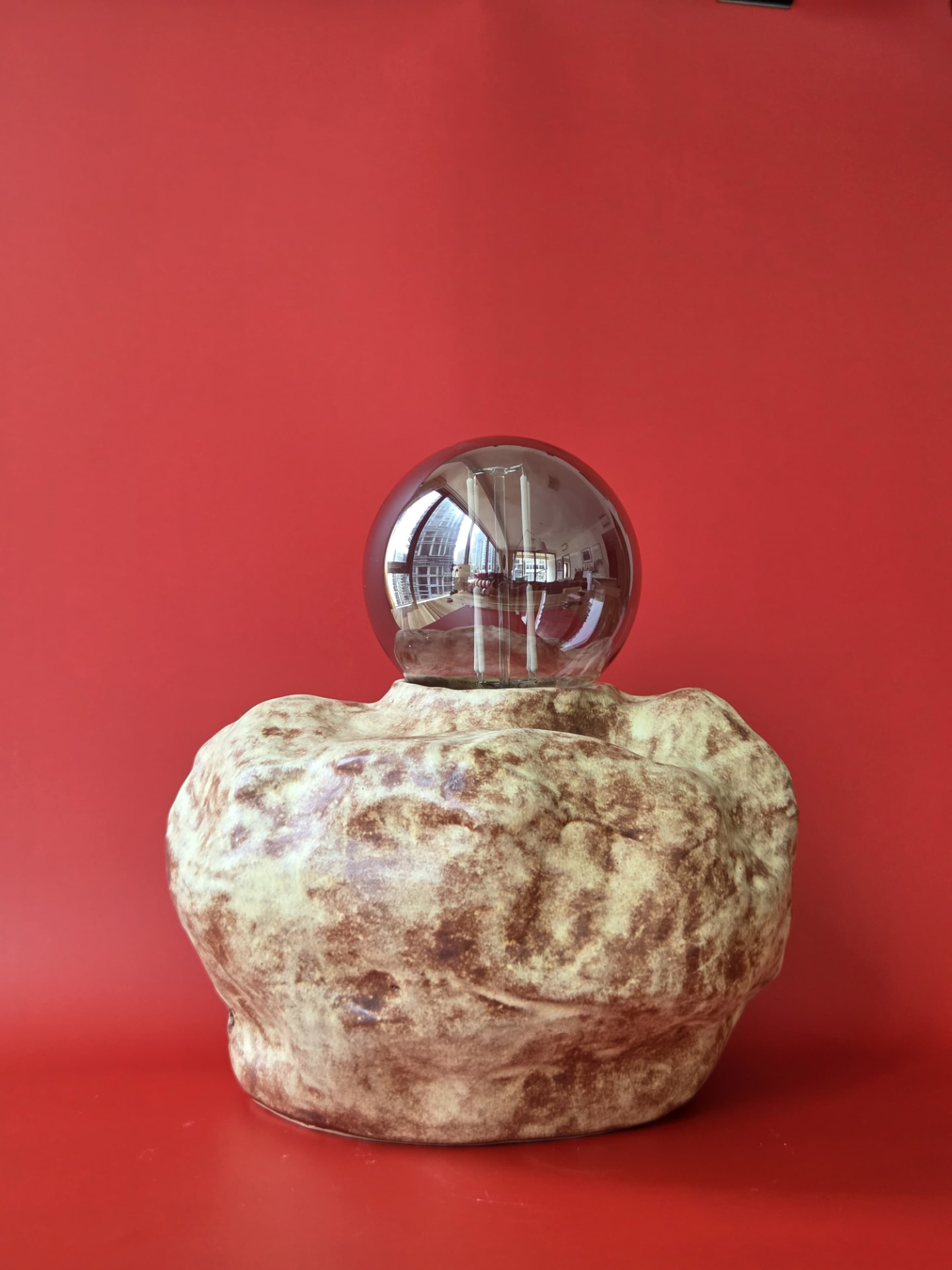 Erratic, a stoneware lamp with a boulder-like form and smoked glass globe against a red backdrop