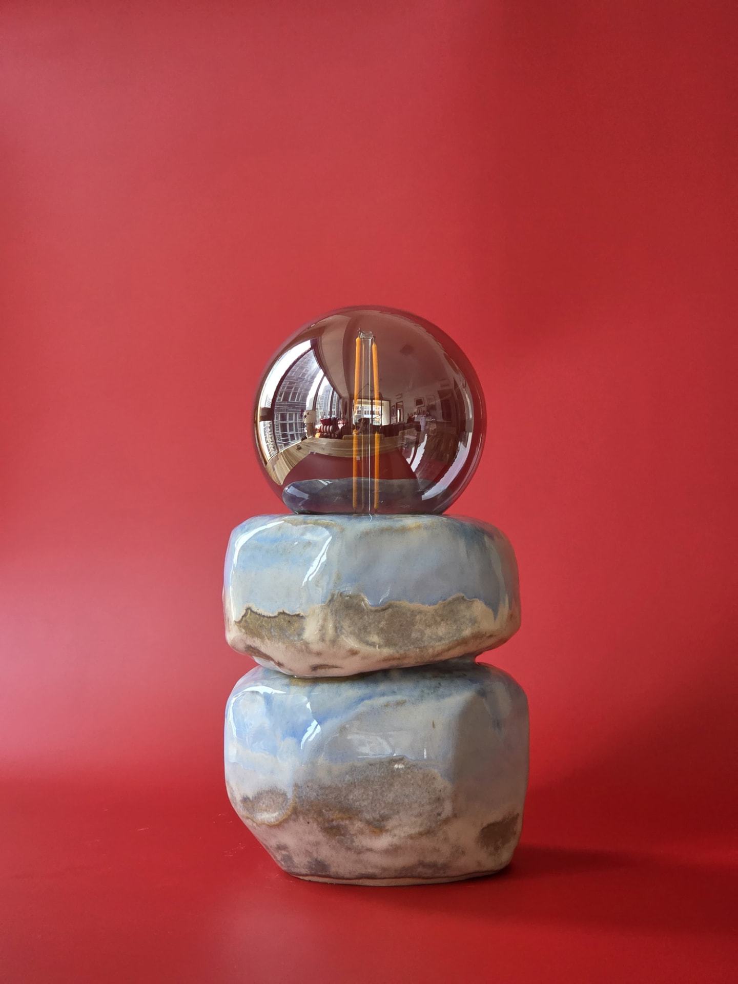 Cairn, a stoneware lamp made from two stacked forms with a smoked glass globe against a red backdrop