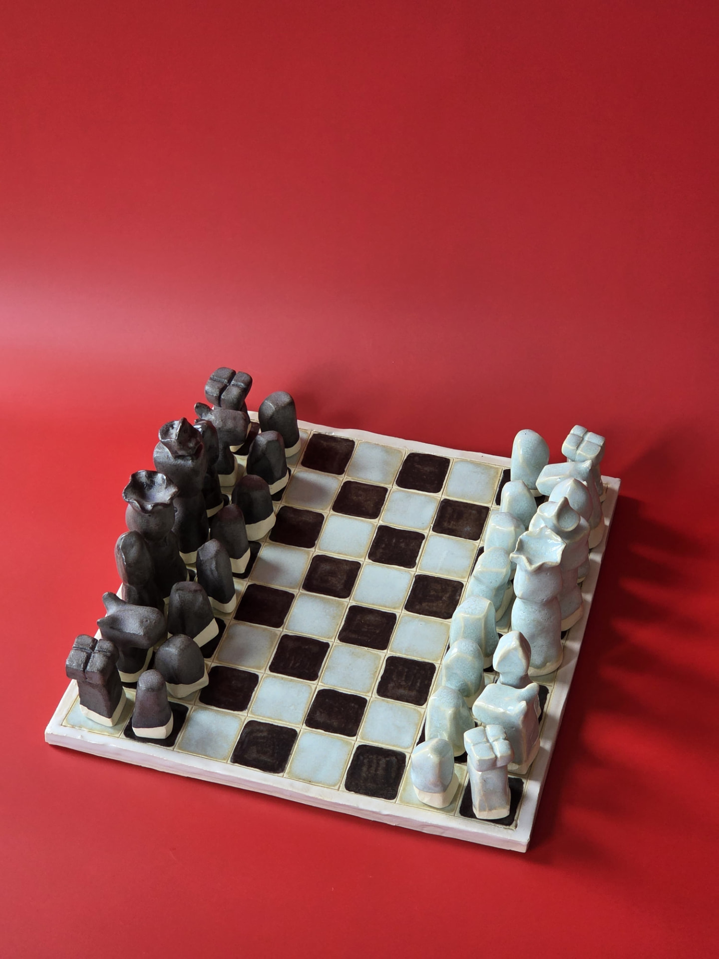 Overhead view of Littoral's full chess set arranged on its glazed checkered board