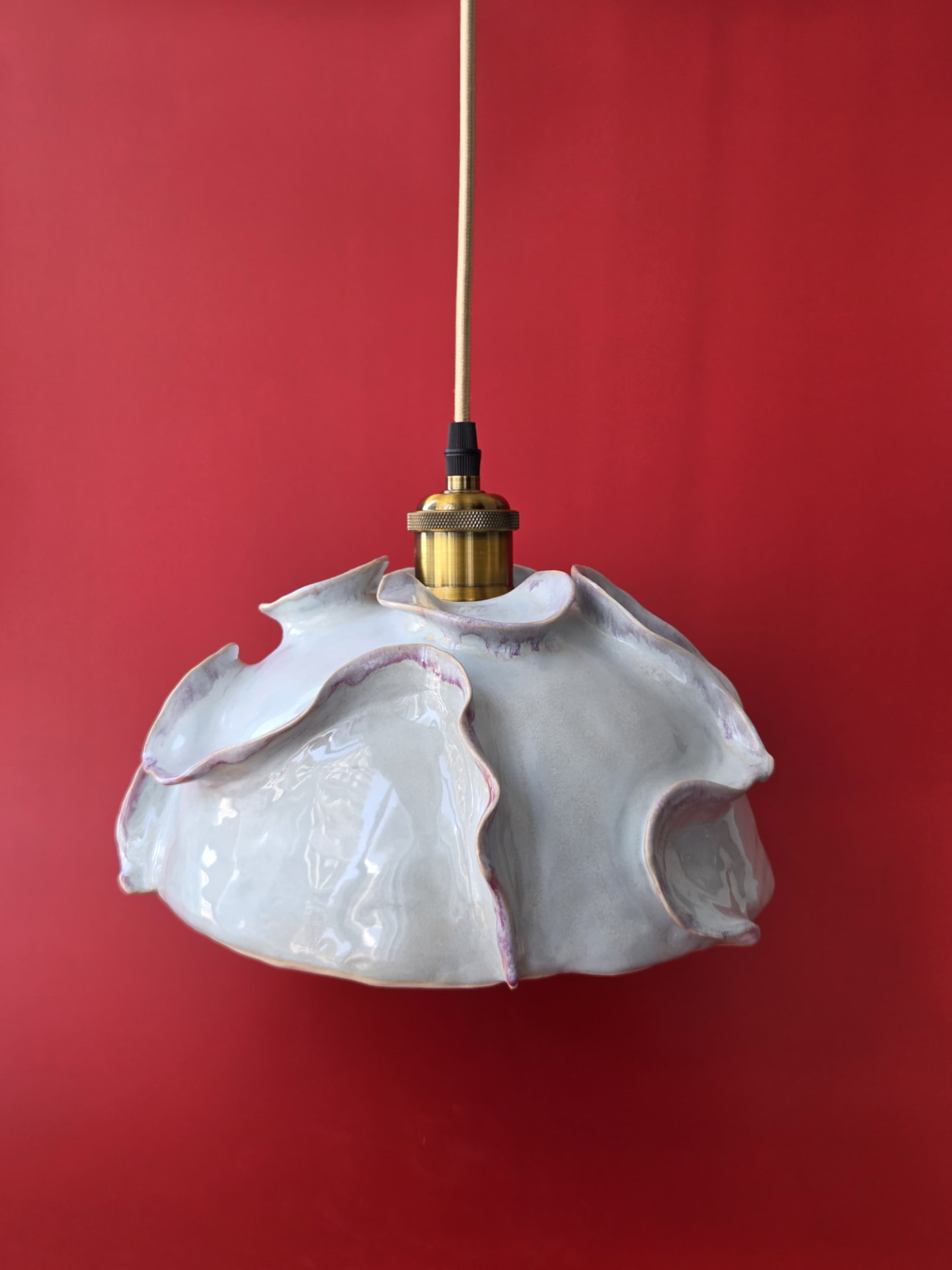 Coralline, a pale-glazed stoneware pendant light with undulating coral-like edges and brass furnishing against a red backdrop