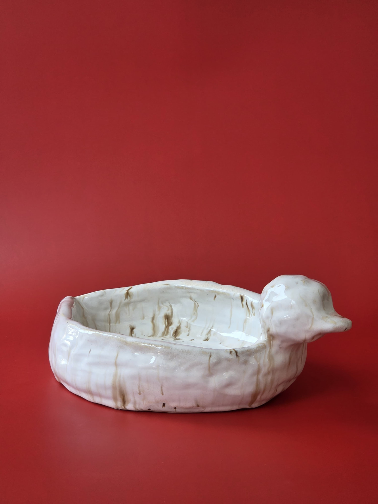 Mooring, a cream-glazed ceramic object shaped like a resting waterbird against a red backdrop