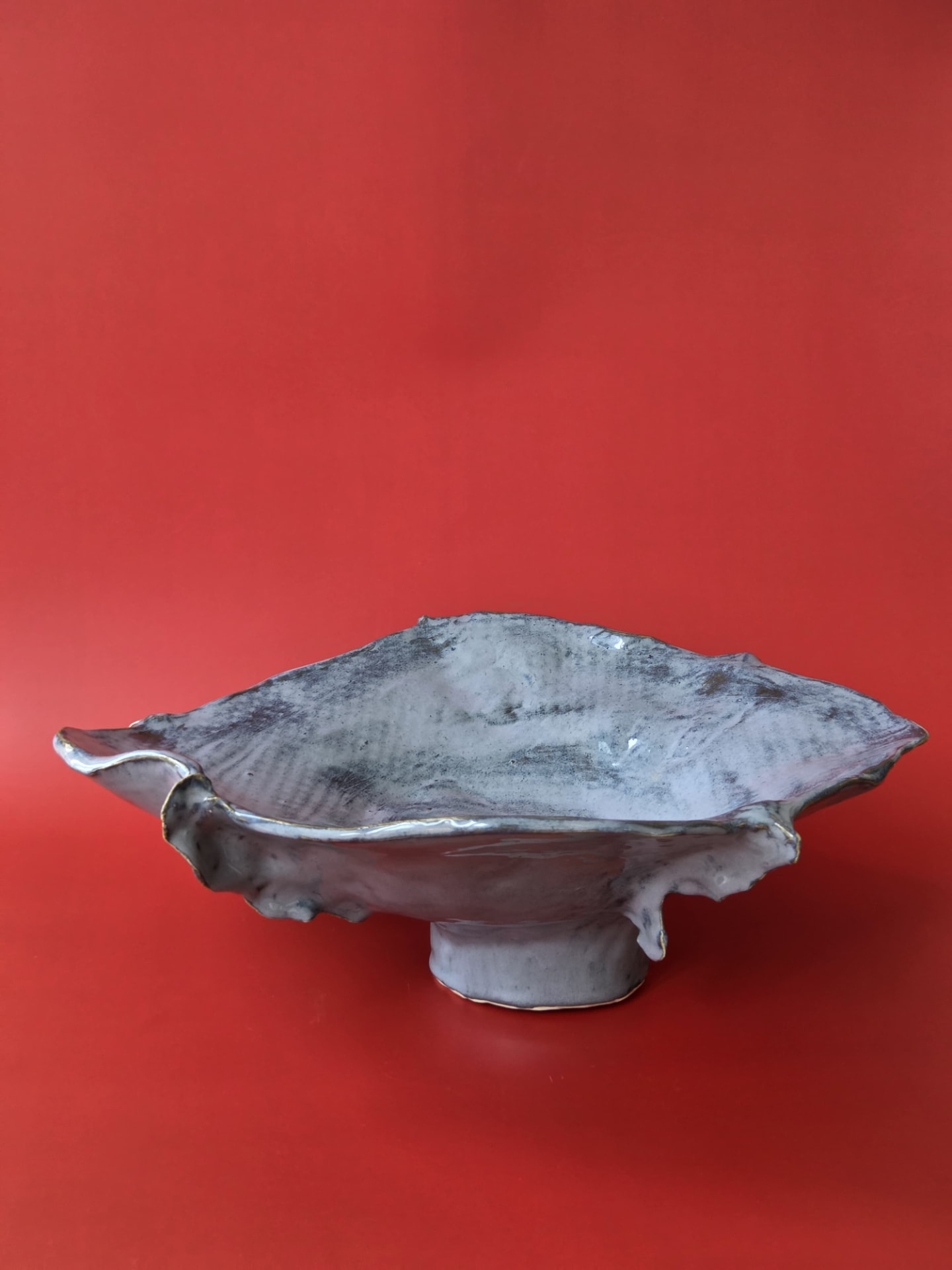 Caldera, a wide grey-glazed ceramic object with a rippled, rising rim against a red backdrop