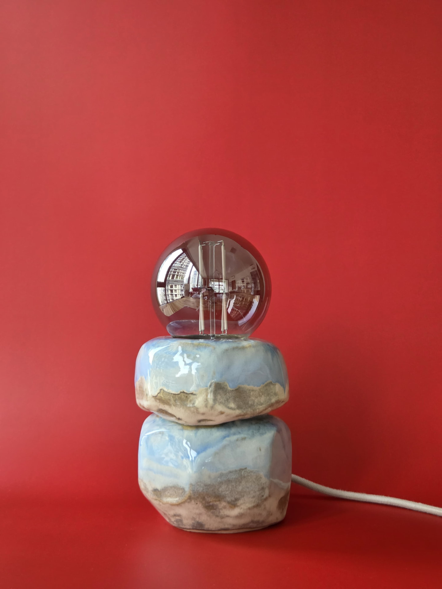 Cairn stoneware lamp with pale blue and sand-coloured glaze against a red backdrop