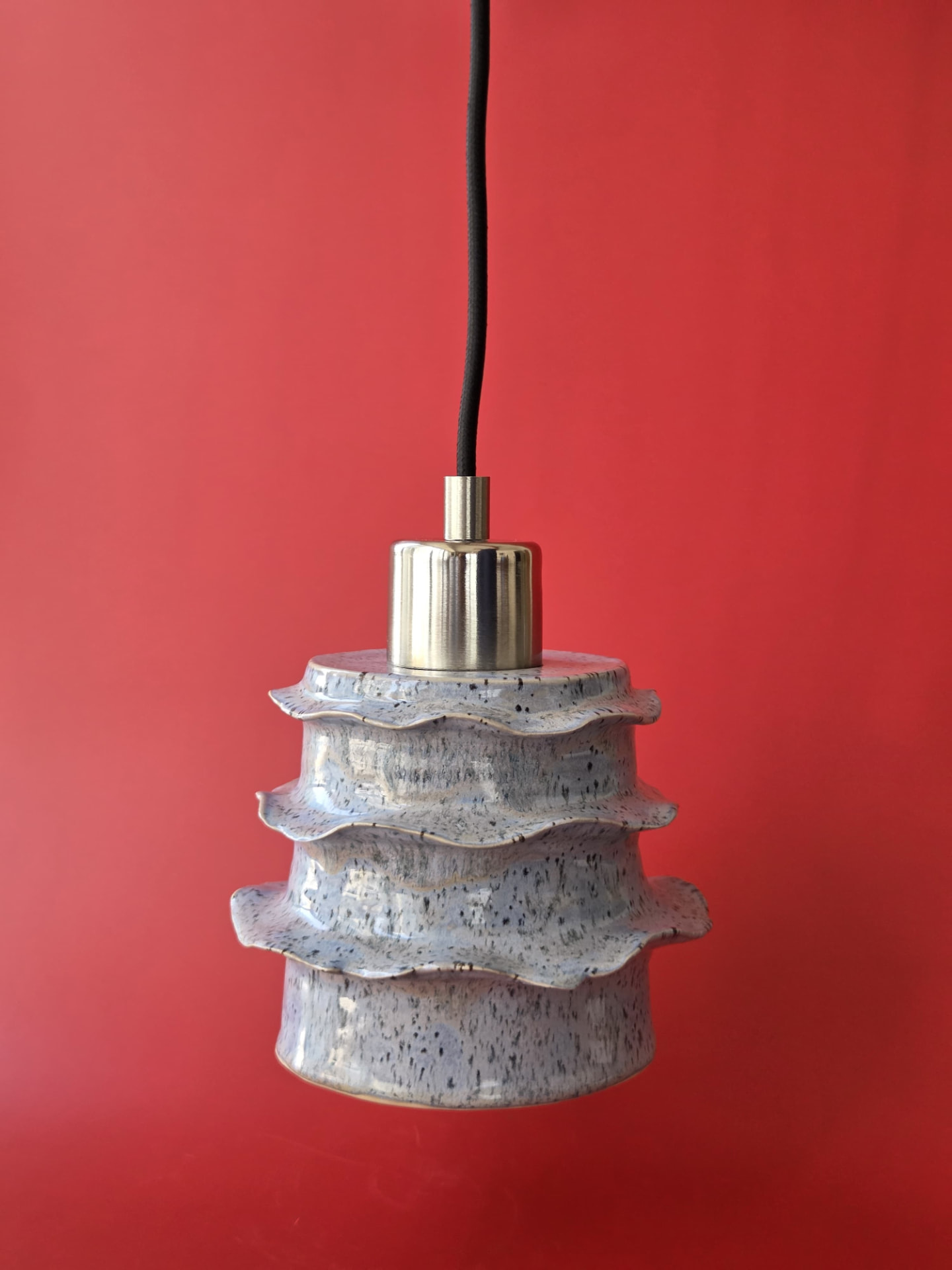 Strata, a three-tiered stoneware pendant light with irregular rim edges and nickel furnishing against a red backdrop