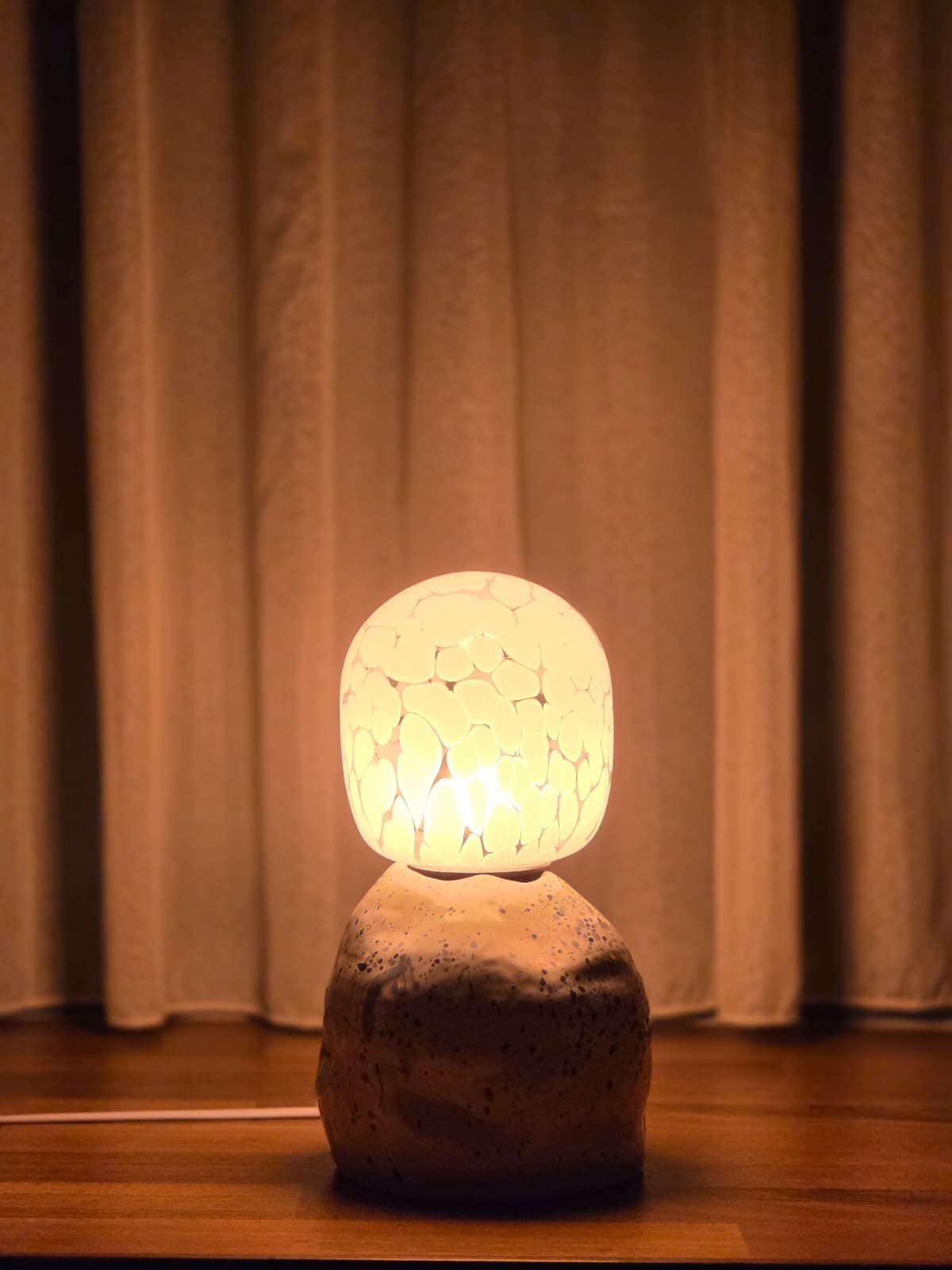Ceramic table lamp glowing warmly against linen curtains
